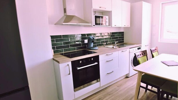 A modern kitchen with white cabinets, a black oven, a green tiled backsplash, and a wooden countertop. - Chez Jean 3 Hyper Centre Wifi 4 Pers Bollaert (Lens)