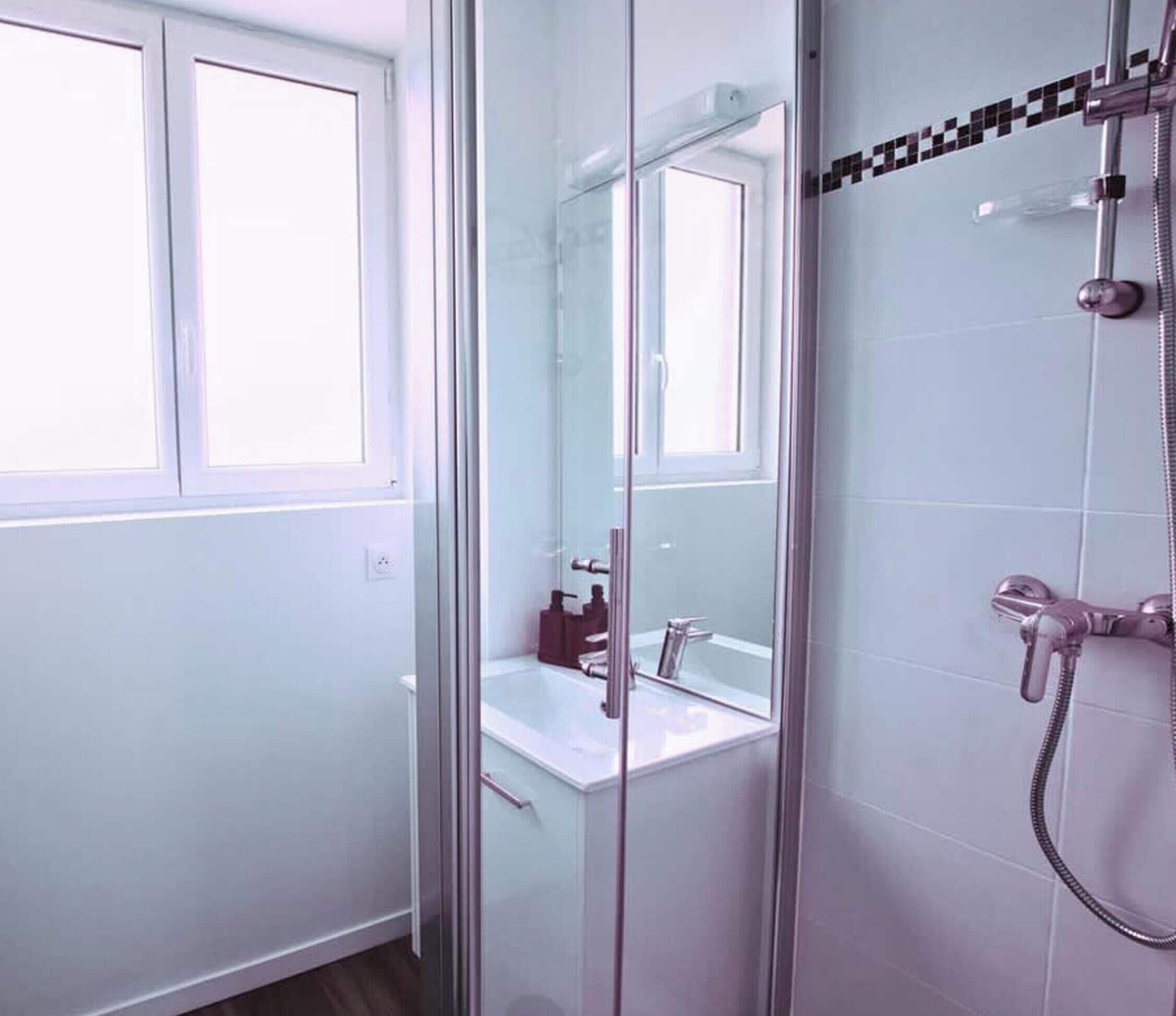 Een moderne badkamer met een douchecabine van glas, een witte wastafel en een spiegel.