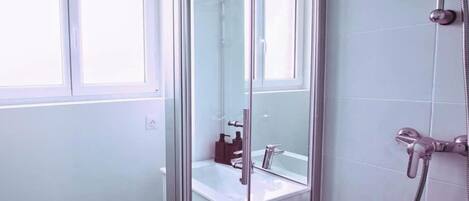 Een moderne badkamer met een douchecabine van glas, een witte wastafel en een spiegel.