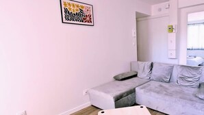 A modern living room with a grey sofa, a small wooden table, and a colorful abstract painting on the wall. - Chez Jean 3 Hyper Centre Wifi 4 Pers Bollaert (Lens)