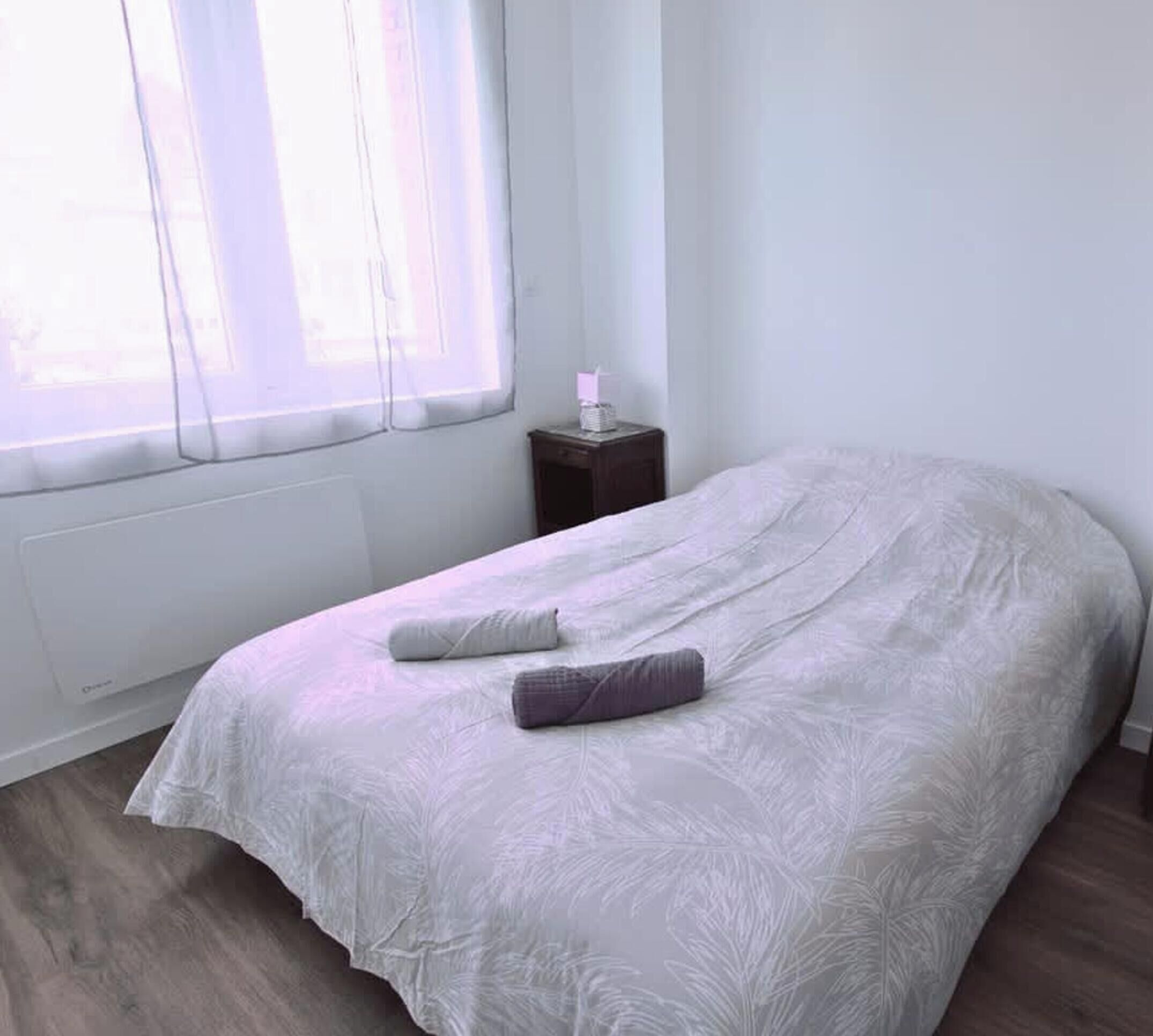 A bedroom with a bed, a nightstand, a window, and a radiator.