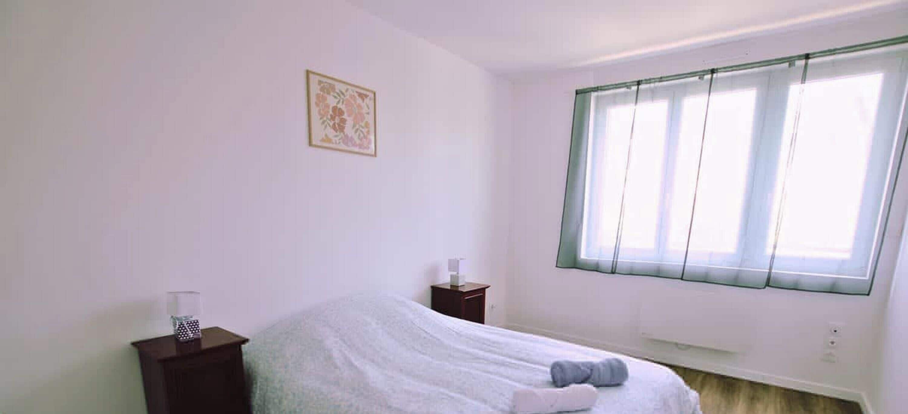 Un dormitorio con cama, una mesita de noche, una ventana con persianas y un cuadro colgado en la pared.