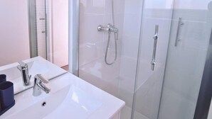 A modern bathroom with a glass-enclosed shower, a white sink with two faucets, and a mirror. - Chez Jean 3 Hyper Centre Wifi 4 Pers Bollaert (Lens)