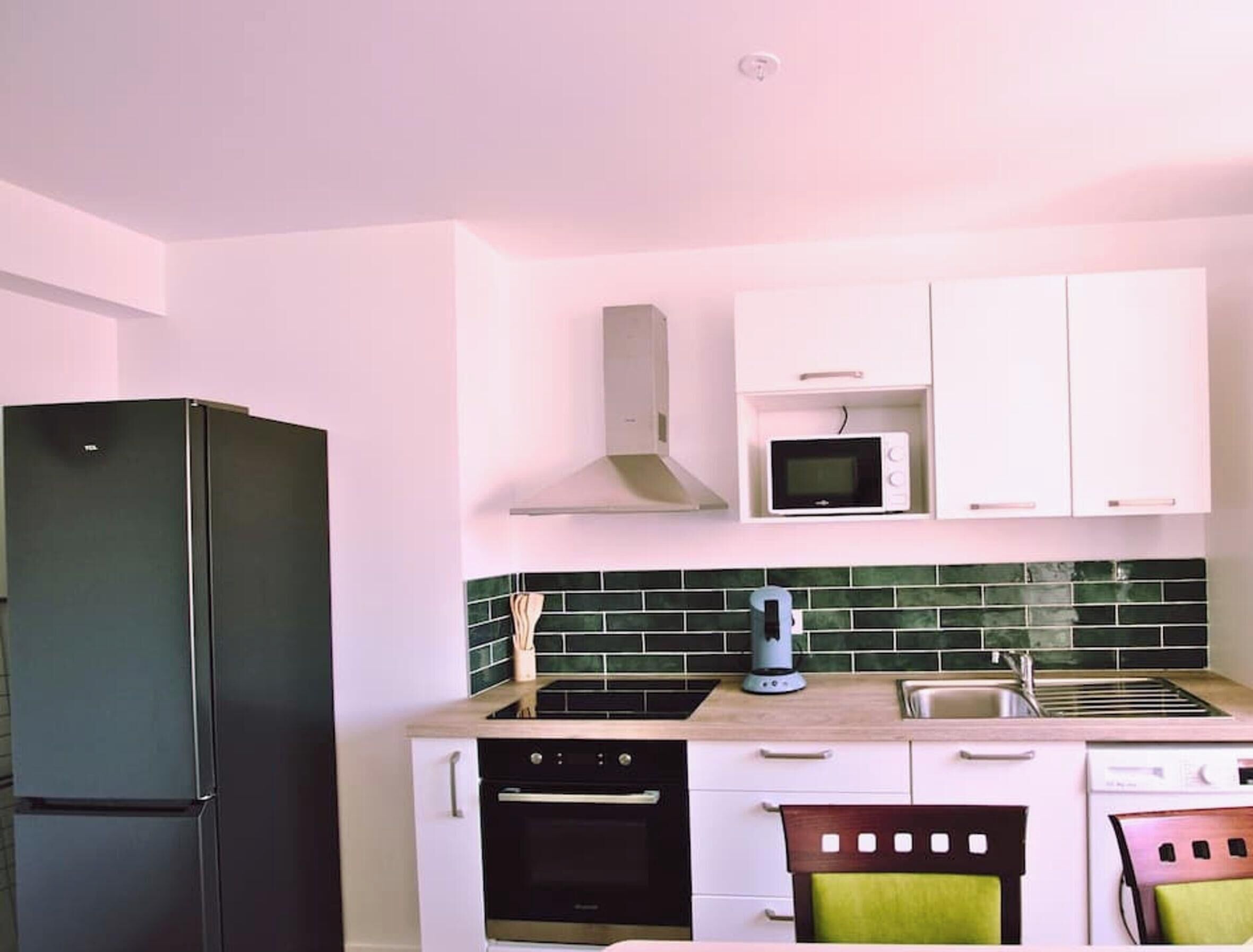 Una cocina con gabinetes blancos, un refrigerador negro, un microondas y una estufa.