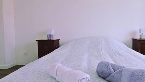 A neatly made bed with a patterned bedspread, two rolled towels, and a small bedside table with a cup and a book. - Chez Jean 3 Hyper Centre Wifi 4 Pers Bollaert (Lens)