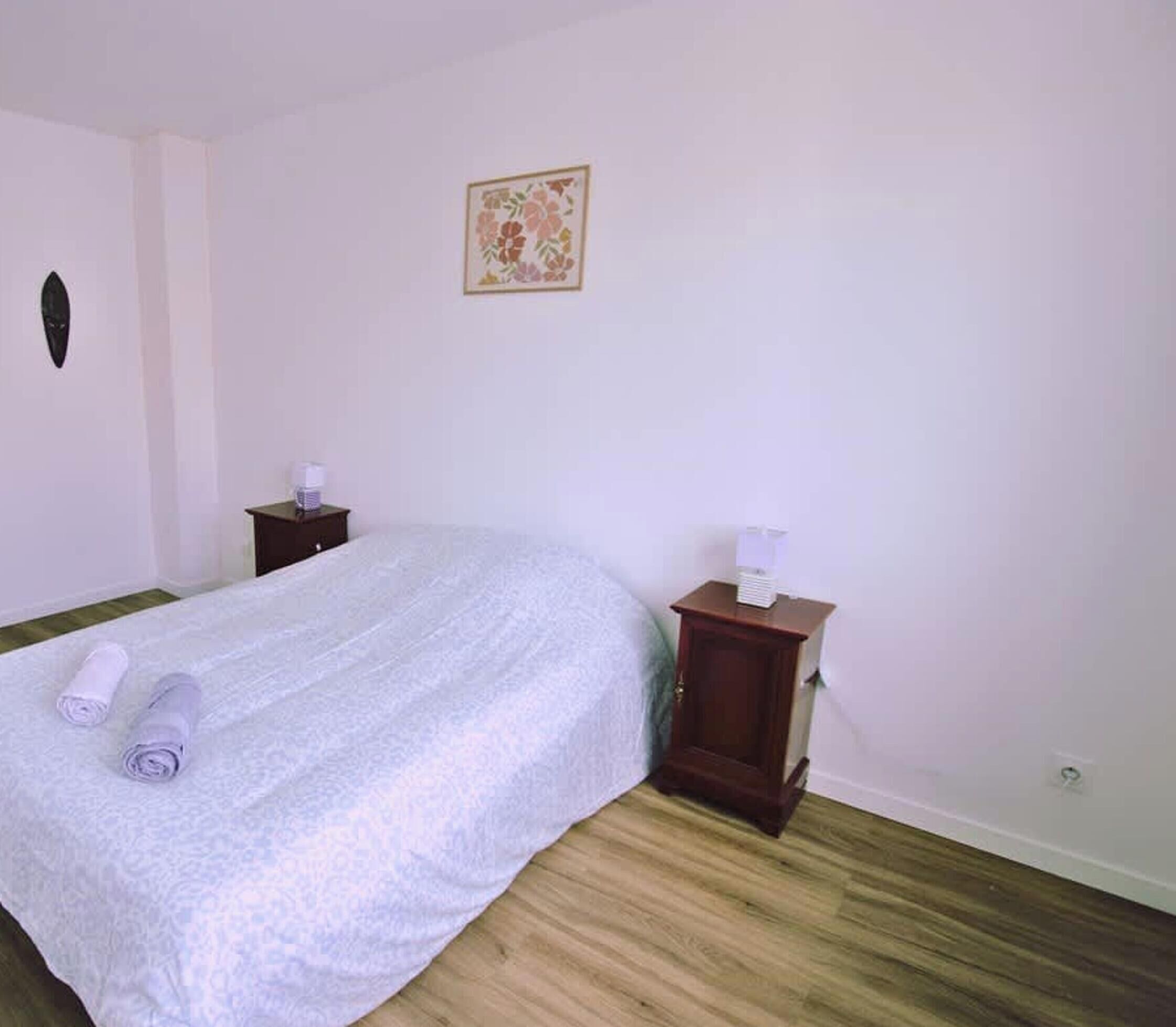 A bedroom with a bed, two nightstands, a wall-mounted light, and a floral artwork.