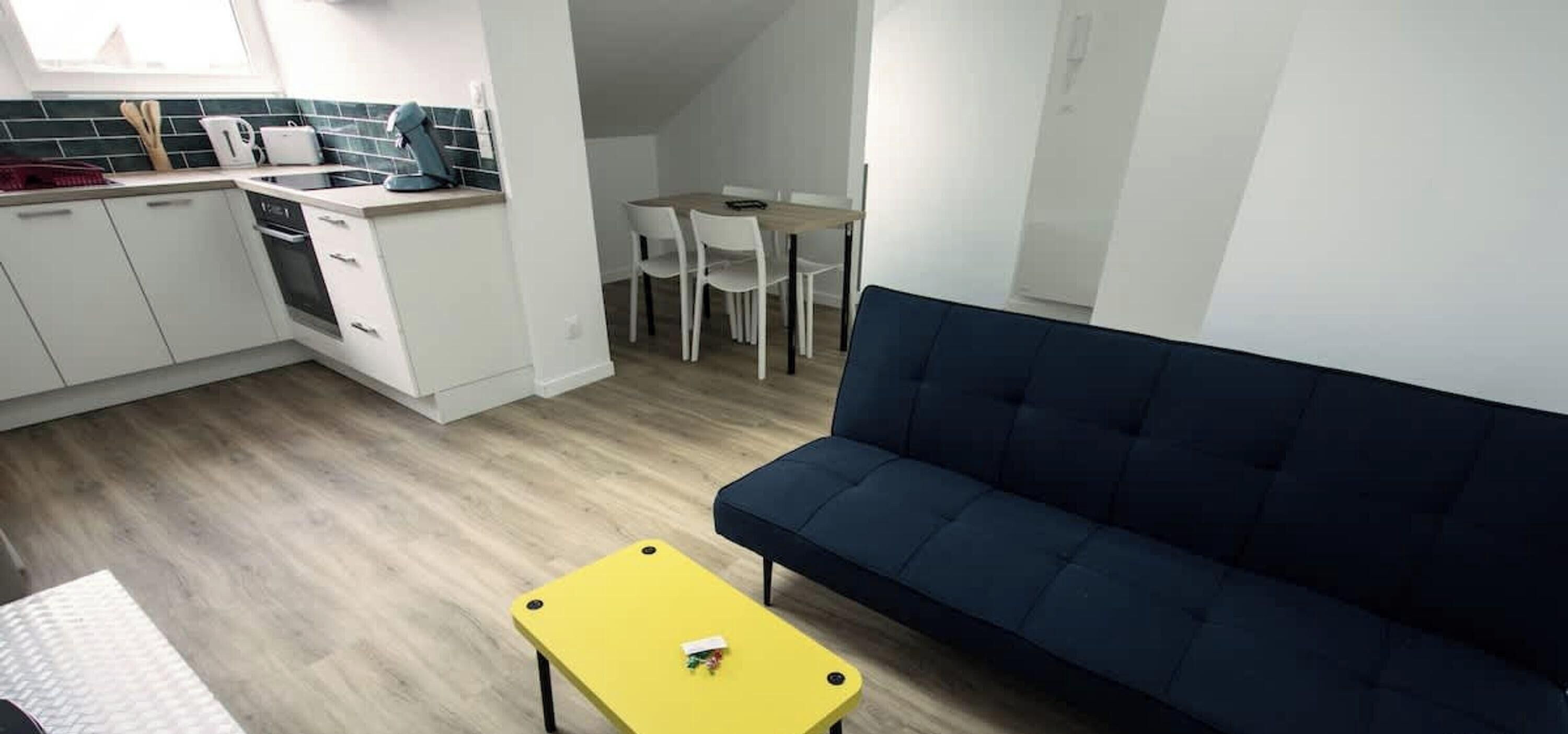 A compact living space with a kitchenette, a dining area, and a dark blue sofa.