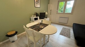 A compact living space with a dining area, a TV, a microwave, and a window with a view of greenery. - Studio Avec Place de Parking (Arras)