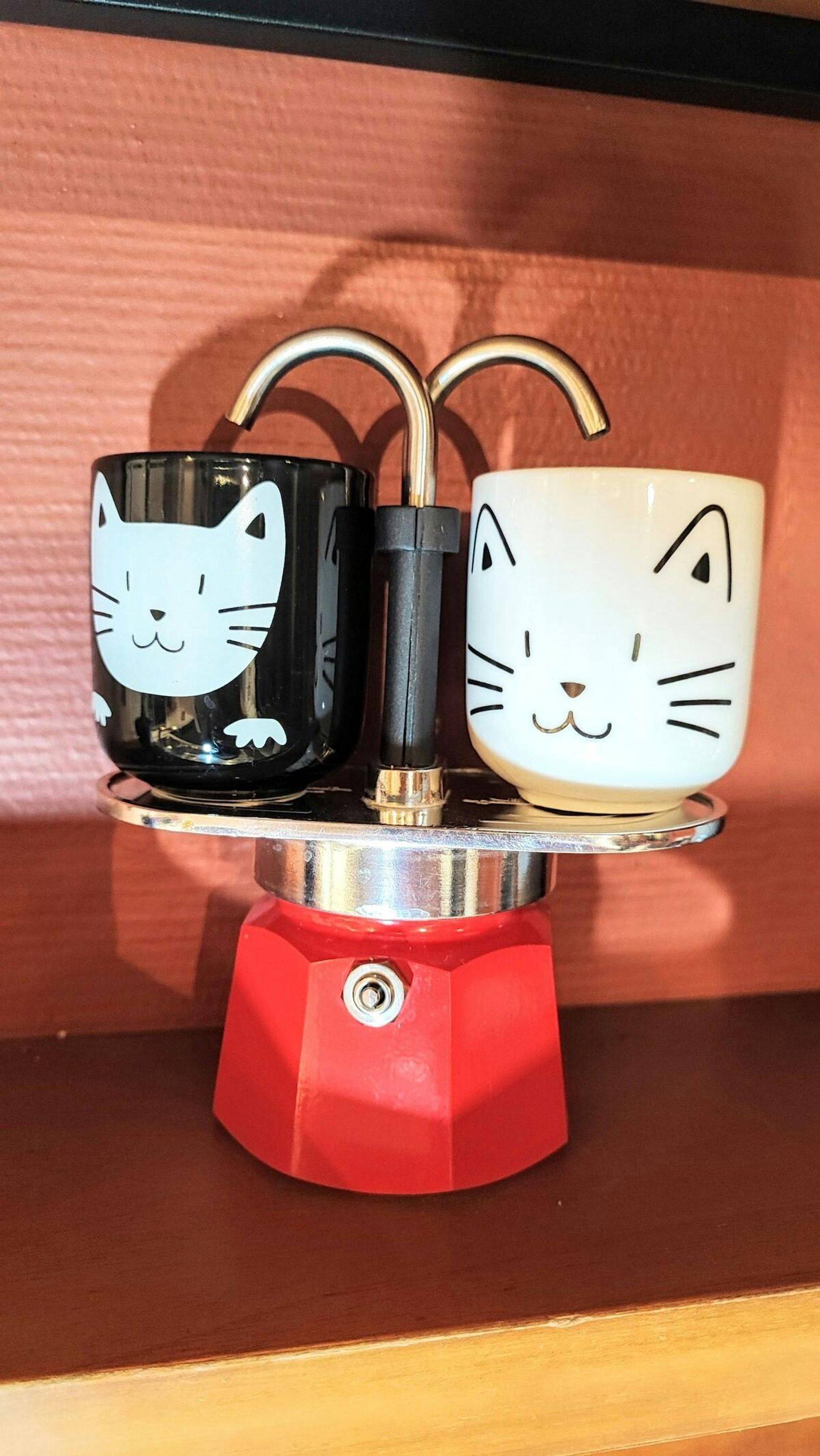 Un présentoir rouge avec deux tasses décorées de motifs de chats.
