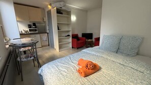 Ein kleines Hotelzimmer mit Bett, einer Küchenzeile, einem Esstisch und einem Fernseher.