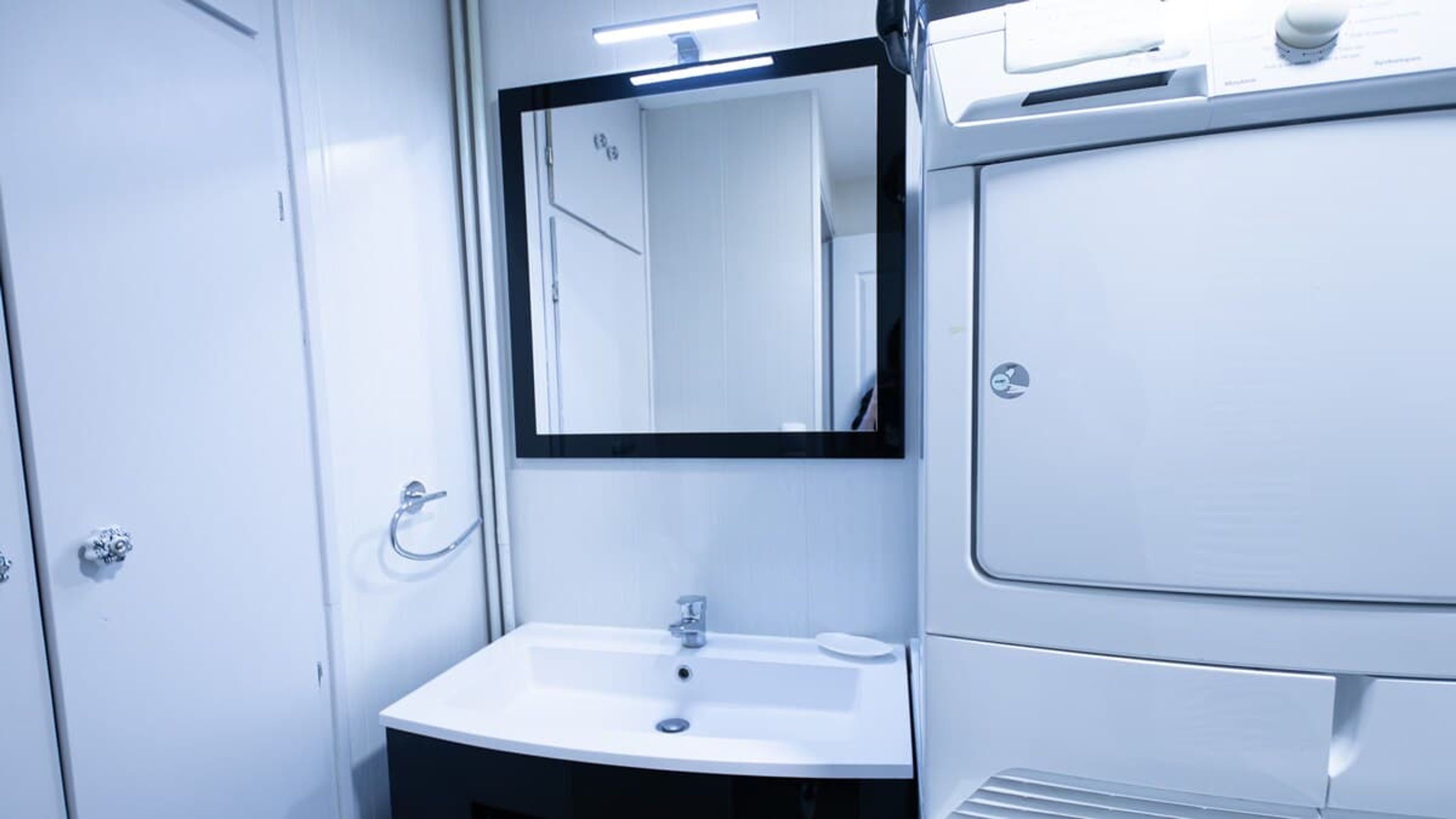 A small, white bathroom with a sink, mirror, and a door.