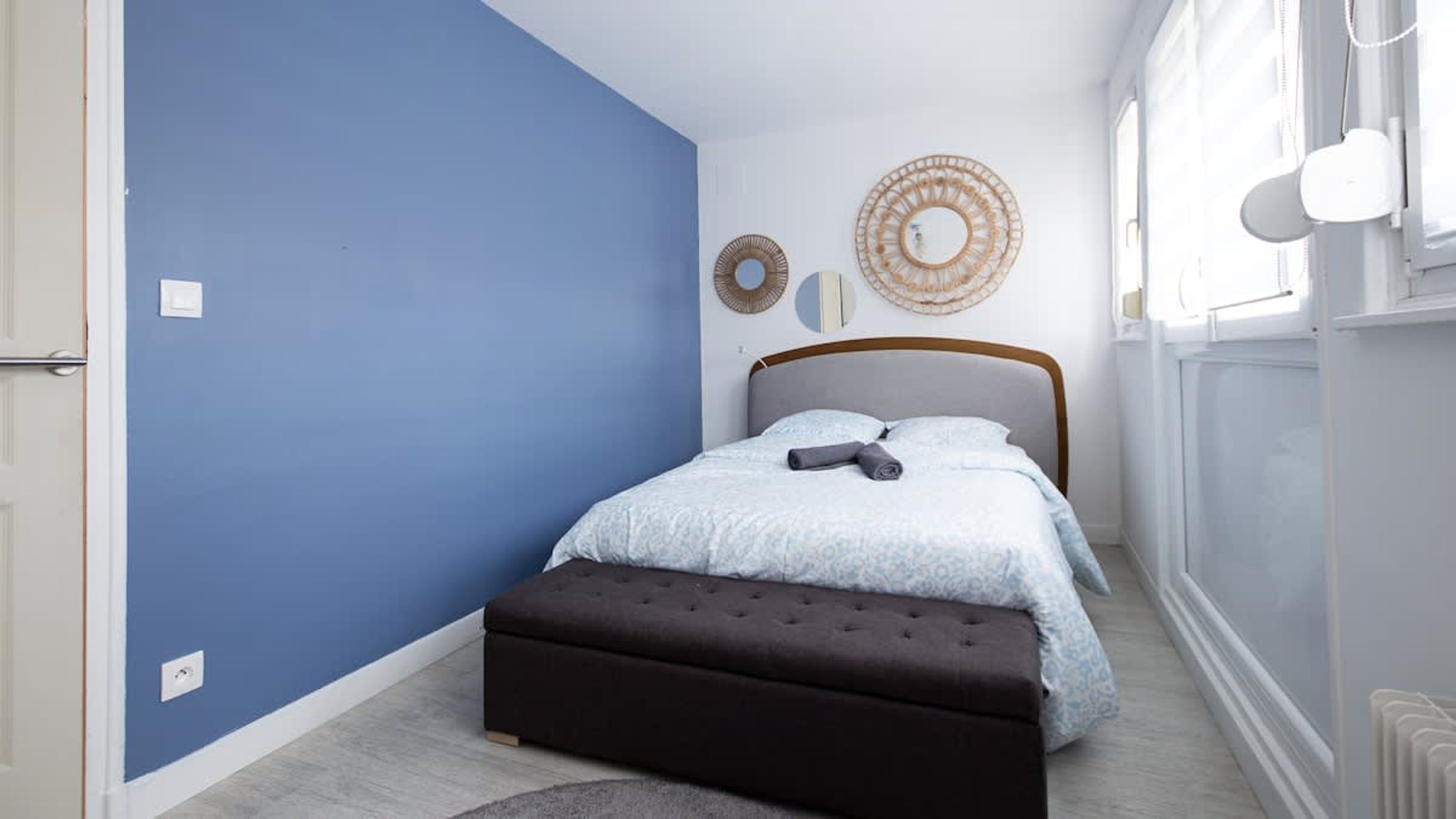 A bedroom with a bed, a dark bench, and a wall with circular decor.