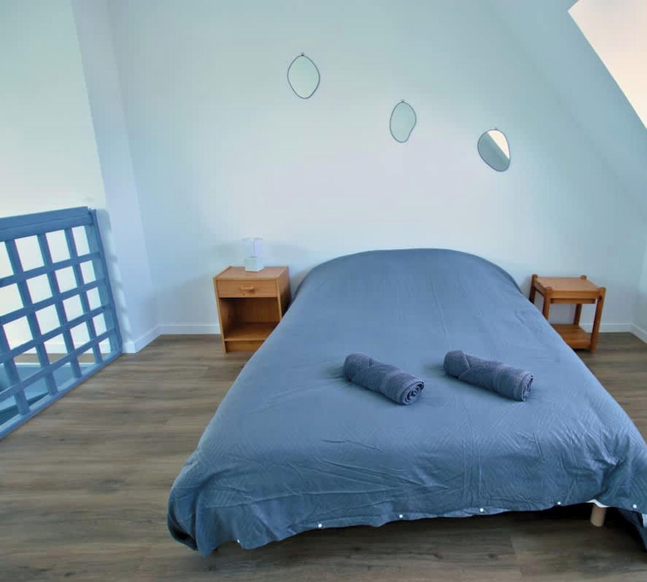 Un dormitorio con una cama, dos mesitas de noche, suelo de madera y techo inclinado.