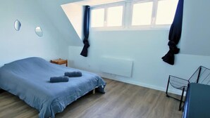 Et soveværelse med skråvæg, en seng, et lille trænatbord, en radiator og et vindue med gardiner.