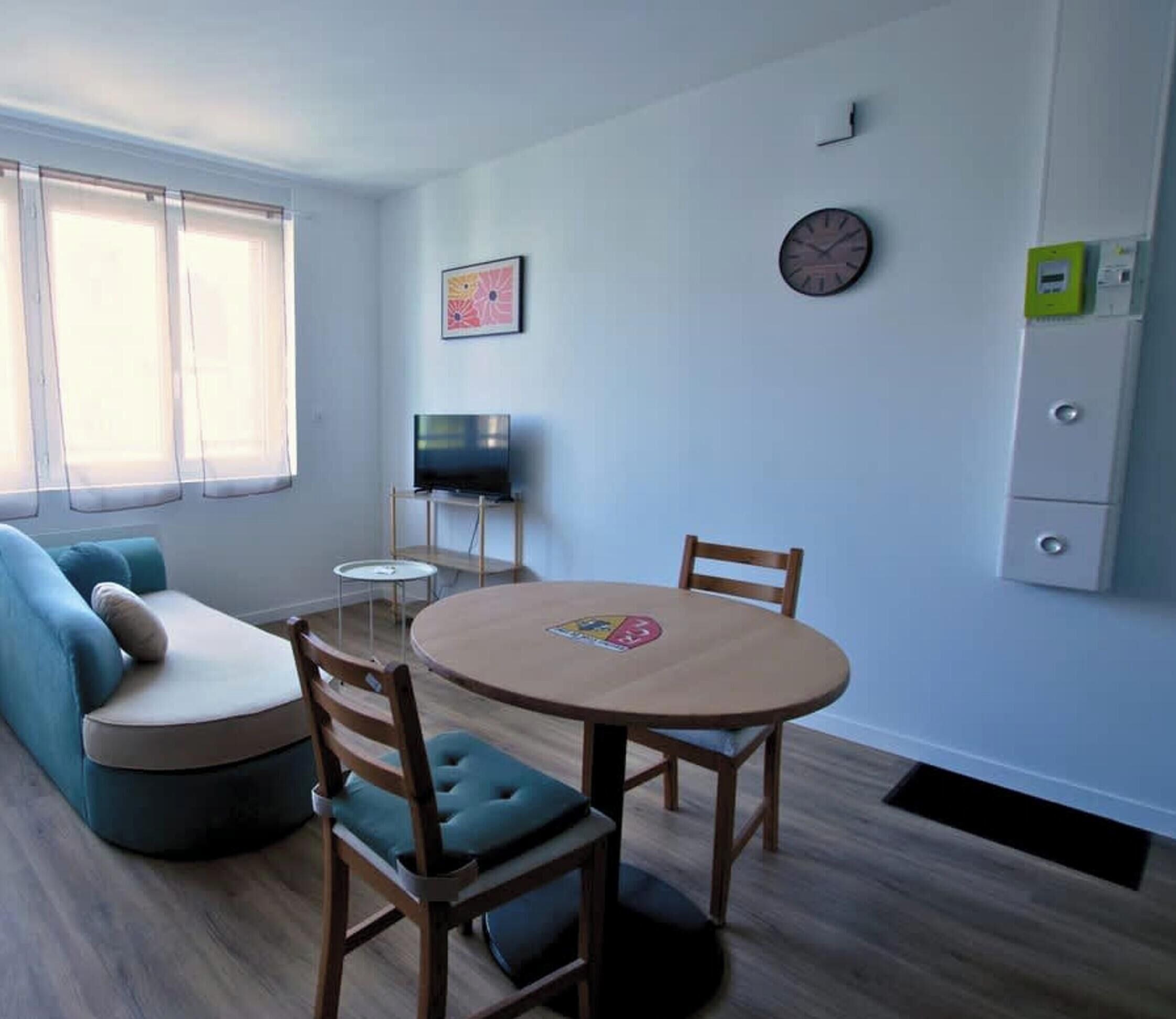 A modern living room with a sofa, a round table, two chairs, a television, and a clock on the wall.