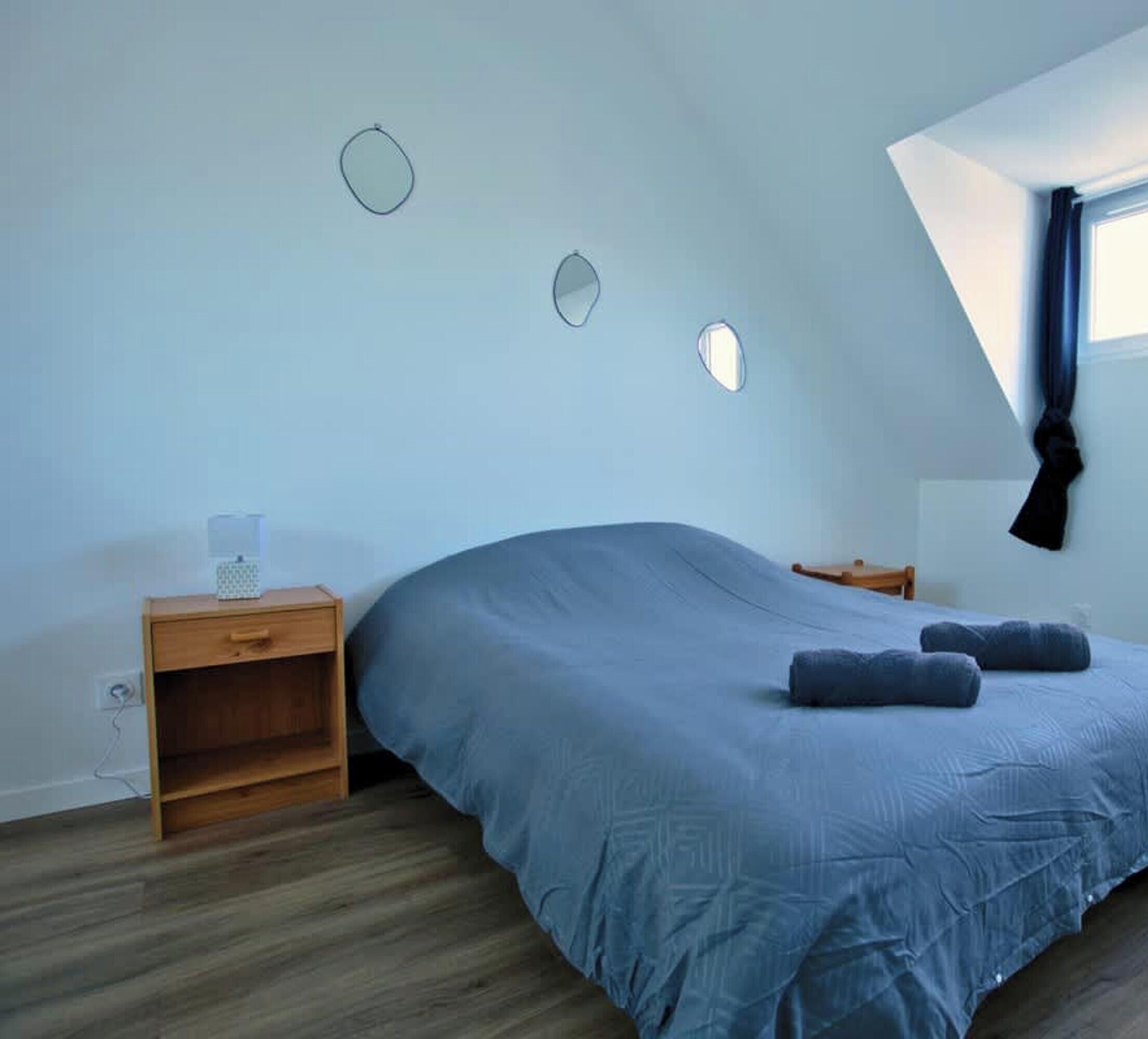 A bedroom with a bed, a nightstand, a window with a curtain, and a sloped ceiling.