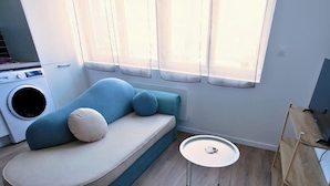 En kompakt opholdsstue med sofa, lille rundt bord, fjernsyn på et stativ og en vaskemaskine.