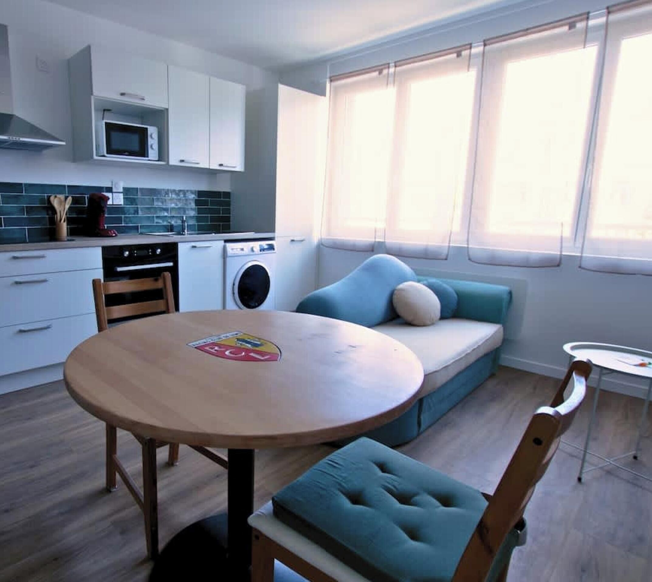 A compact living space with a kitchenette, a sofa with cushions, a round wooden table, and a small round table.
