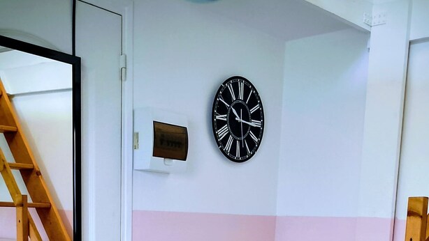 Une pièce avec un escalier en bois, une porte blanche et une horloge murale.