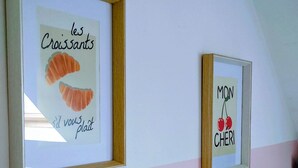 Deux tableaux encadrés sont accrochés au mur : l’un représente un croissant accompagné d’un texte, l’autre, des cerises, également accompagné d’un texte.