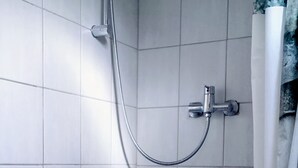 Un espace douche avec des murs recouverts de carreaux blancs, une pomme de douche et un drain.