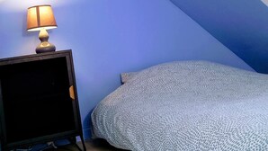 Une chambre avec un plafond en pente, une table de chevet avec une lampe et une couvre-lit à motifs.