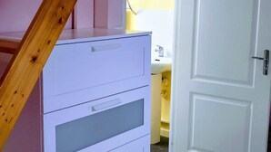 Une pièce avec un escalier en bois, une commode blanche et une porte donnant sur une salle de bain.