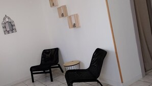 A room with two black chairs, a small round table, and a wall-mounted wooden shelf with three items. - Chez Serge N 107 Jardin Parking Animaux 4 Pers (Noeux-les-Mines)