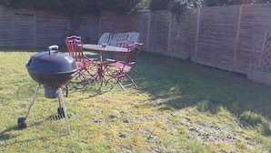 A backyard with a barbecue grill, a table, and red chairs. - Chez Serge N 107 Jardin Parking Animaux 4 Pers (Noeux-les-Mines)