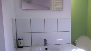 Une salle de bain avec un lavabo blanc, un miroir au-dessus et des toilettes sur la droite.