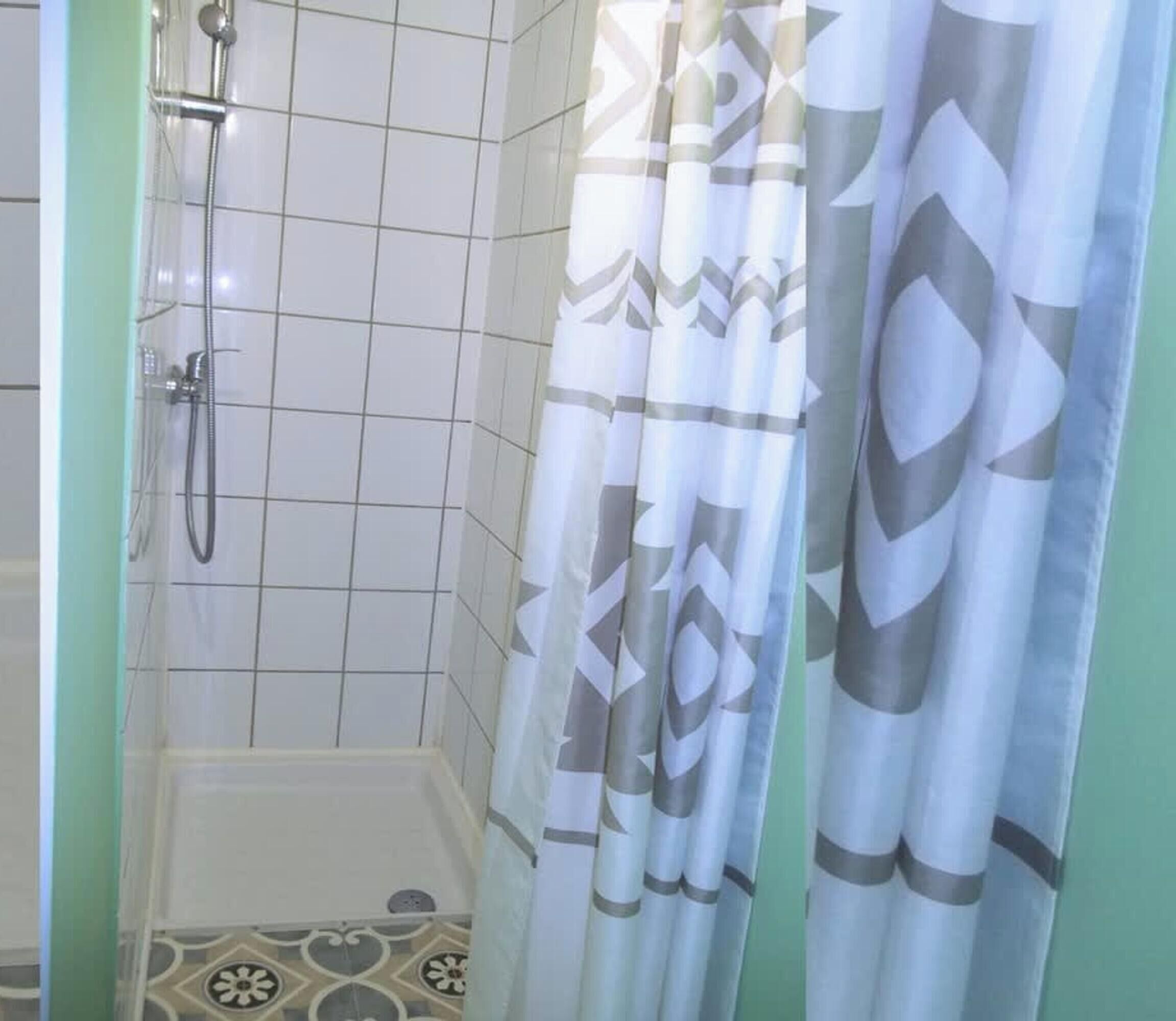 A shower area with a showerhead and hose, tiled walls, and a patterned shower curtain.