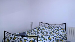 Un lit simple avec un cadre en métal, une couvre-lit à motifs et un luminaire fixé au mur.