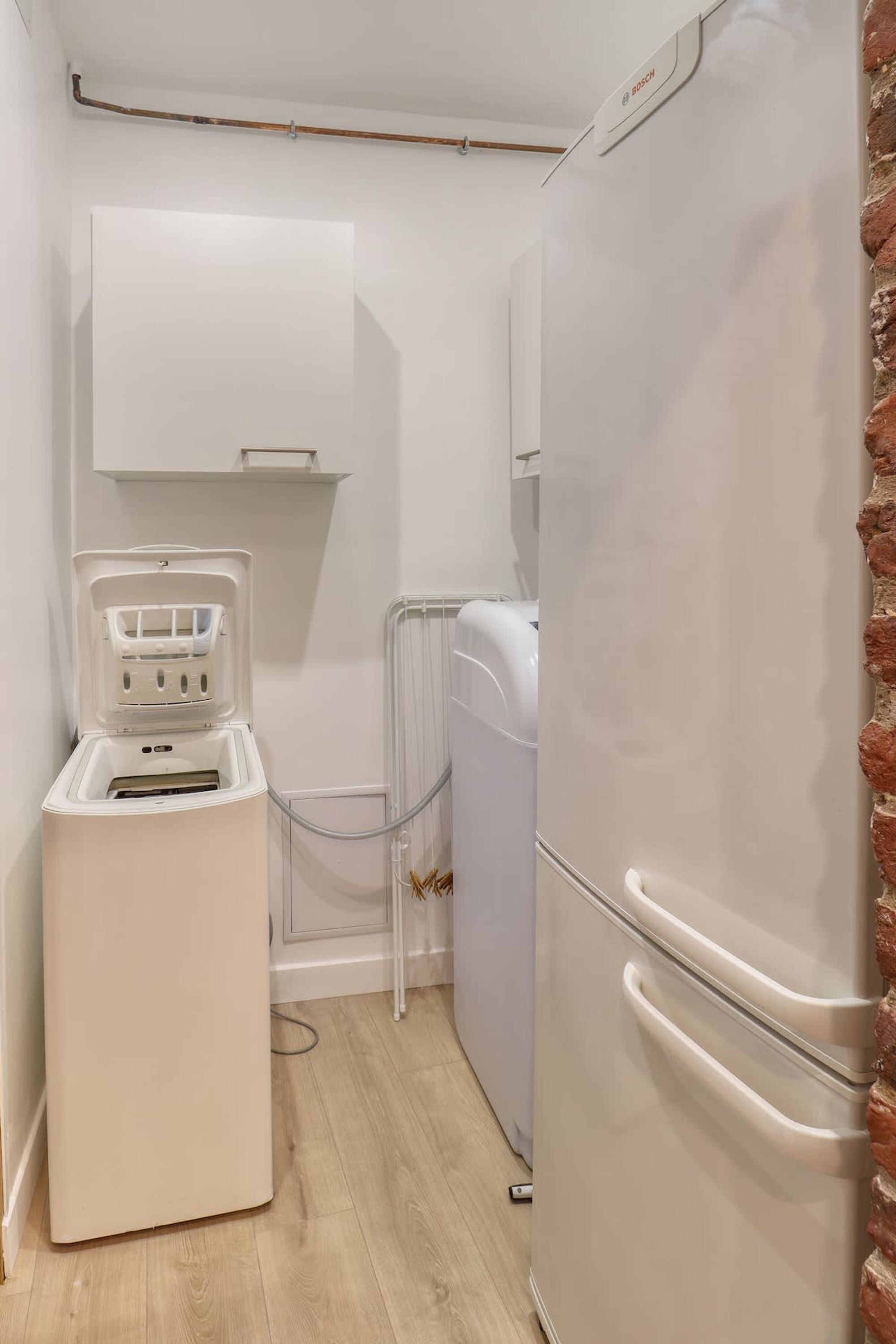 Cocina compacta con un refrigerador blanco, lavadora y un mueble pequeño.