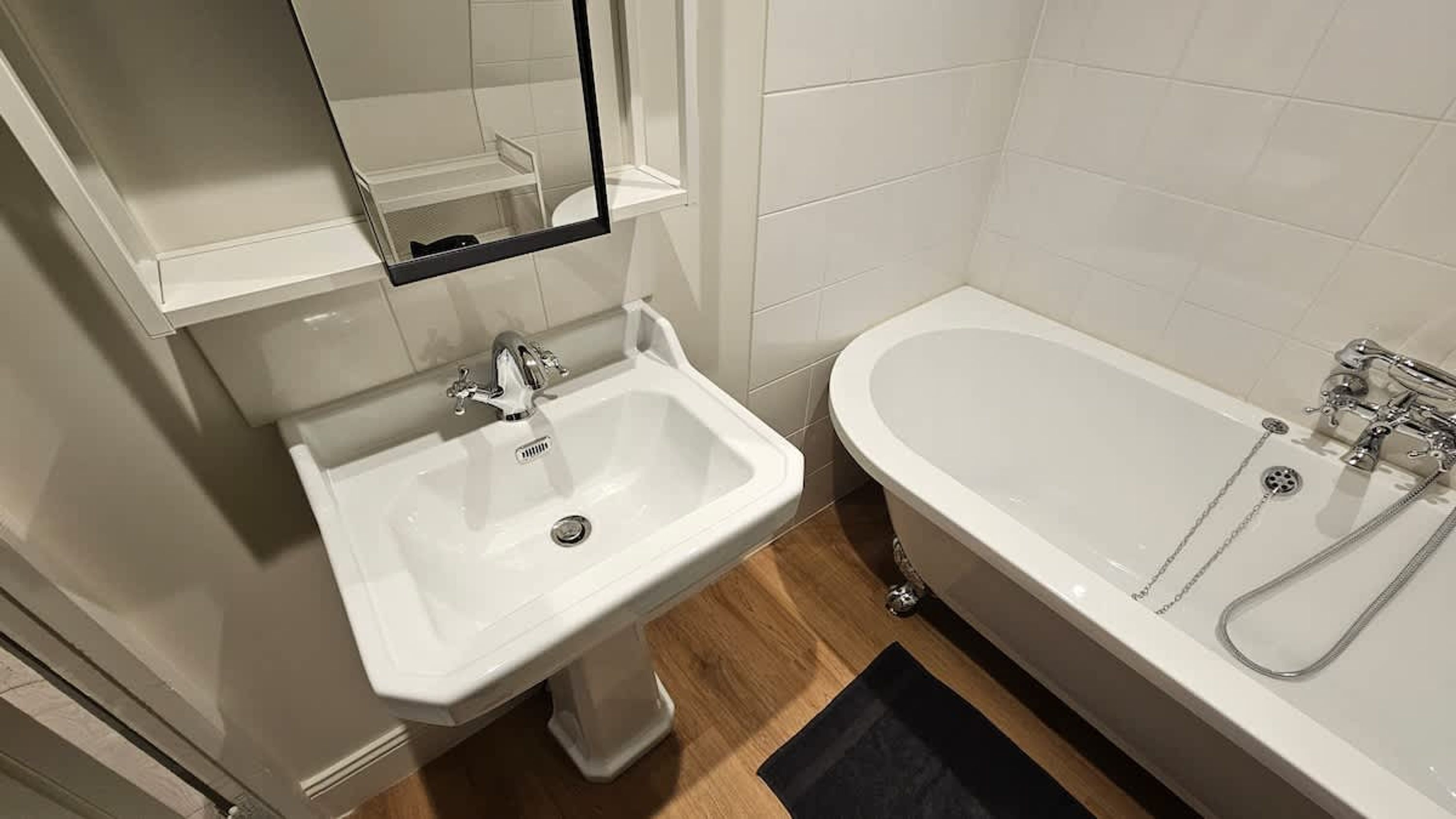 A bathroom with a white sink, a mirror above it, and a bathtub with a showerhead.