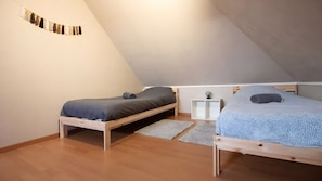 Ein kleines Schlafzimmer im Dachgeschoss mit zwei Holzbetten, einem weißen Nachttisch und einer wandmontierten Leuchte.