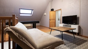 Um quarto com sofá, mesa de bilhar, televisão e janela.