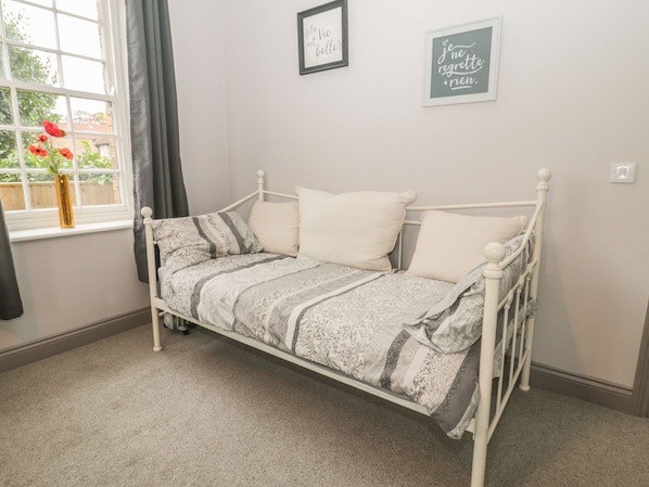 A white metal bed with patterned bedding, a window with curtains, and two wall-mounted signs. - The Sea Chest (Alnwick)