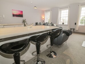 A modern kitchen with a bar area, bar stools, a dining table, and a painting on the wall. - The Sea Chest (Alnwick)