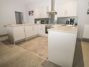 A modern kitchen with white cabinetry, a central island, a stove, and a coffee maker. - The Sea Chest (Alnwick)