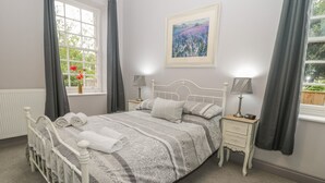Un dormitorio con cama, mesitas de noche, ventana con cortinas, radiador y un cuadro enmarcado en la pared.