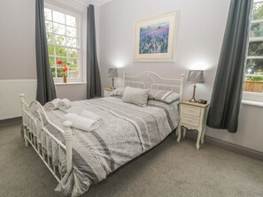 A bedroom with a bed, bedside tables, a window with curtains, a radiator, and a framed picture on the wall. - The Sea Chest (Alnwick)