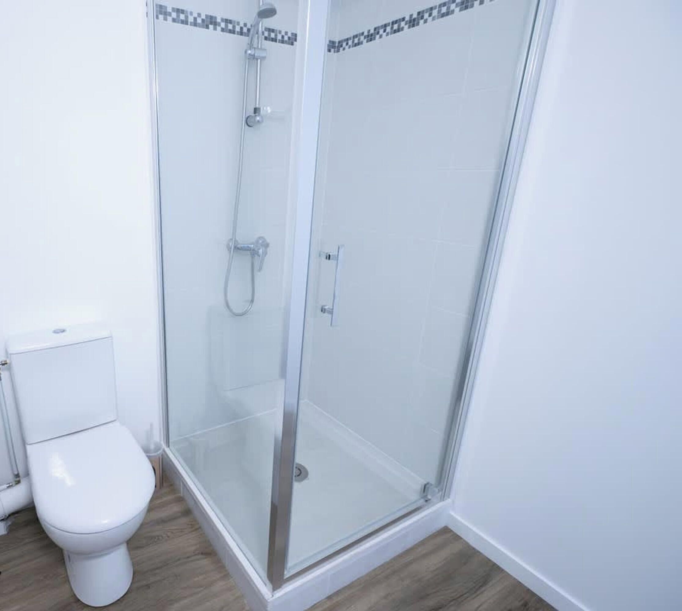 Een badkamer met een glazen douchecabine, een wit toilet en een betegelde vloer.