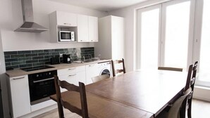 A modern kitchen with white cabinets, a microwave, a stove, and a dishwasher. There is a wooden dining table with chairs. - Chez Jean Hyper Centre 4 Chambres Wifi 8 Pers (Lens)
