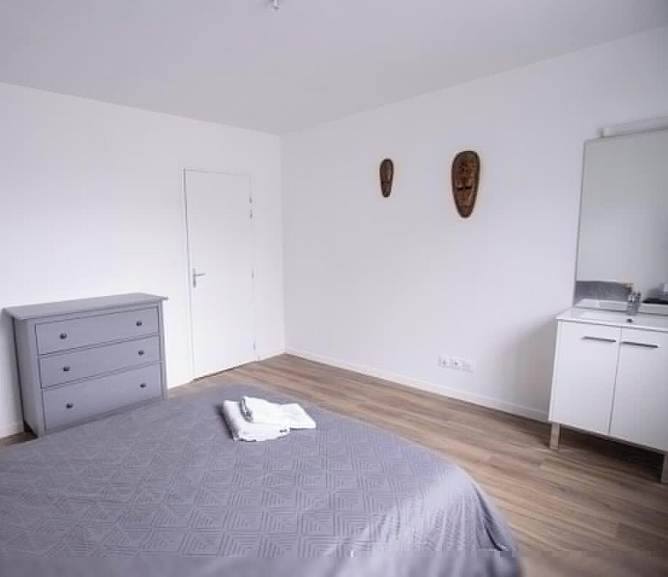 Une chambre à coucher avec un lit, une commode, un miroir et une porte.