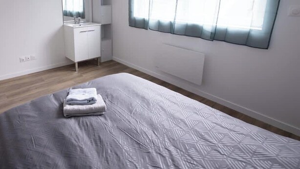 A bedroom with a bed, a bedside table, a mirror, a window with curtains, and a radiator. - Chez Jean Hyper Centre 4 Chambres Wifi 8 Pers (Lens)