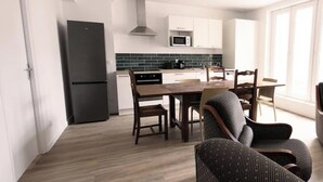 A modern kitchen with white cabinets, a black refrigerator, and a microwave. There is a dining area with a wooden table and chairs. - Chez Jean Hyper Centre 4 Chambres Wifi 8 Pers (Lens)