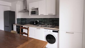 A compact kitchen with white cabinets, a microwave, a washing machine, and a dining table. - Chez Jean Hyper Centre 4 Chambres Wifi 8 Pers (Lens)