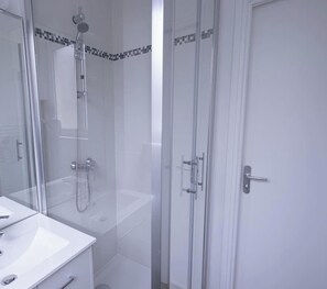 Un baño moderno con ducha de vidrio, un lavabo blanco y una puerta con pomo.
