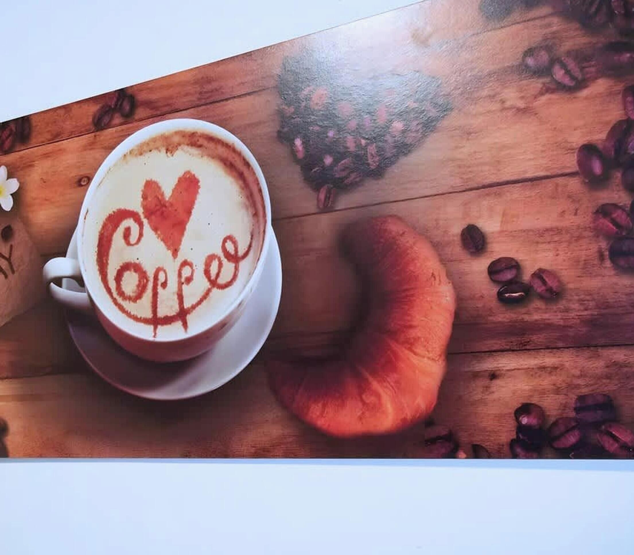 A cup of coffee with a heart and the word 'Coffee' on a wooden surface with scattered coffee beans.