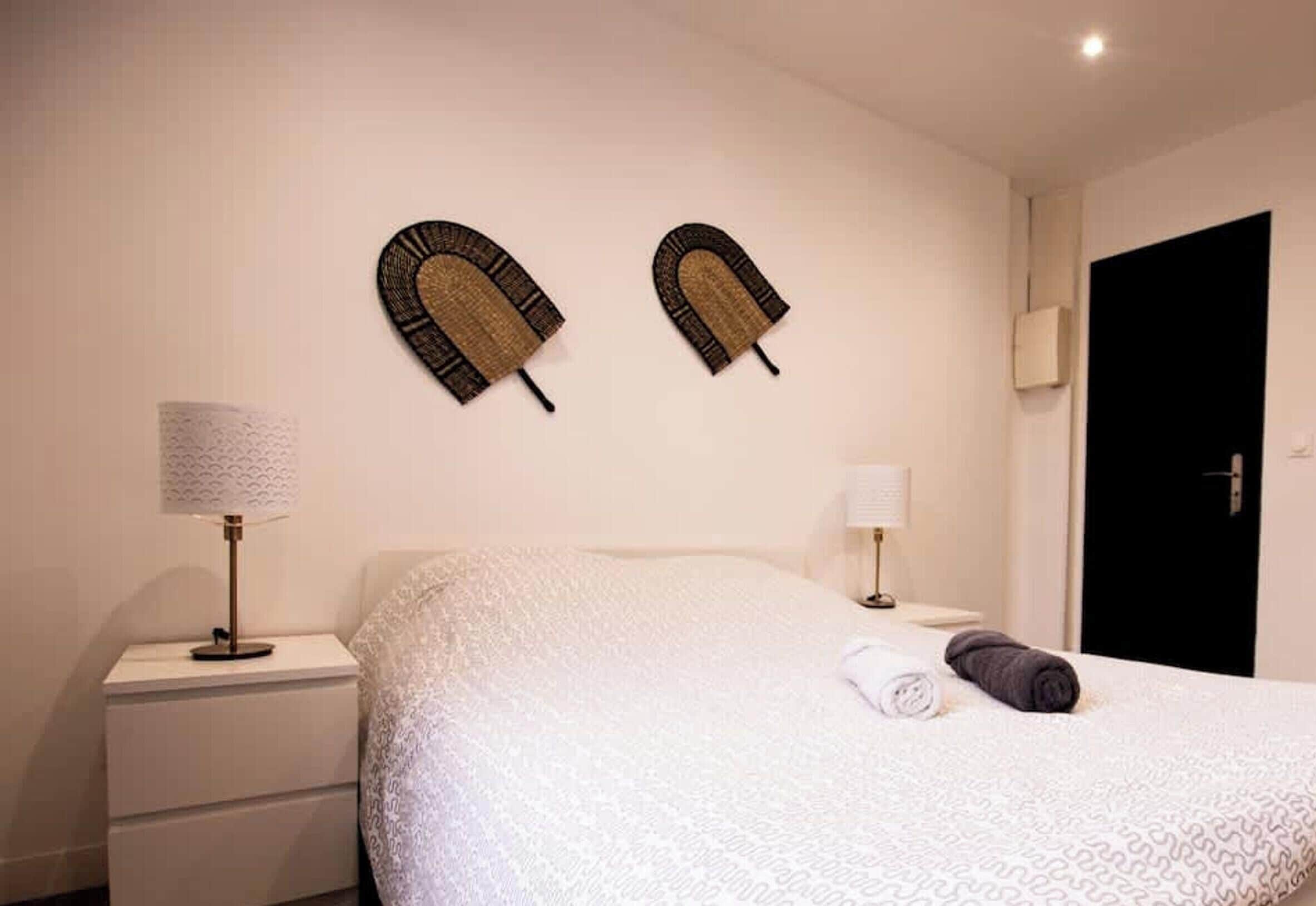 A hotel room with a bed, two wall-mounted lamps, a door, and a nightstand with a lamp.